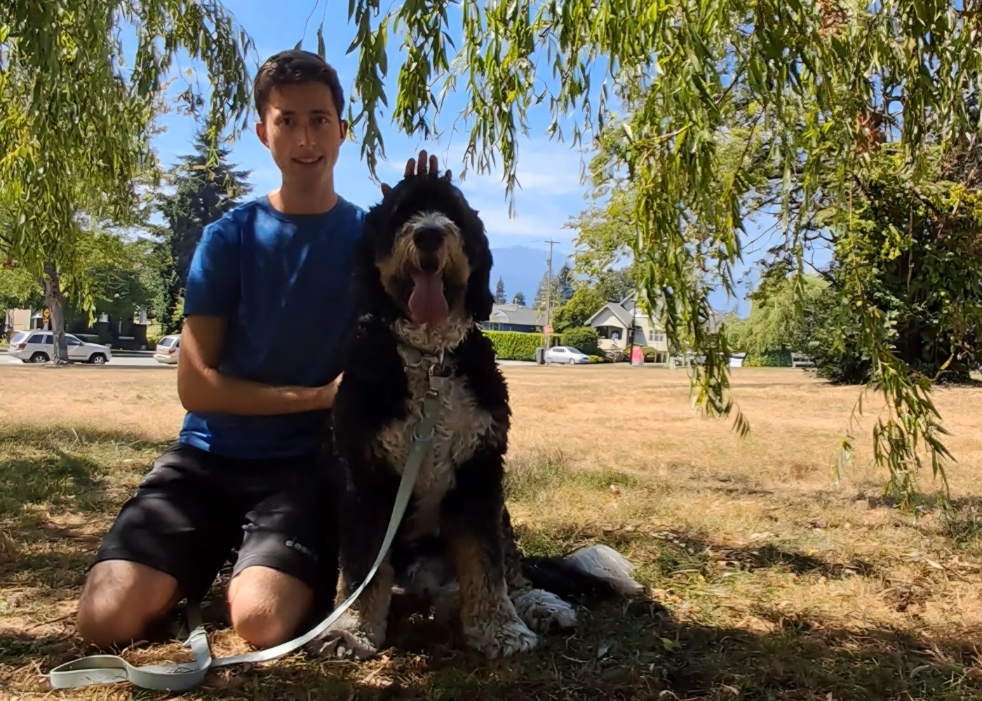 Lukas und ein Hund sitzen unter einem Baum im Grünen.