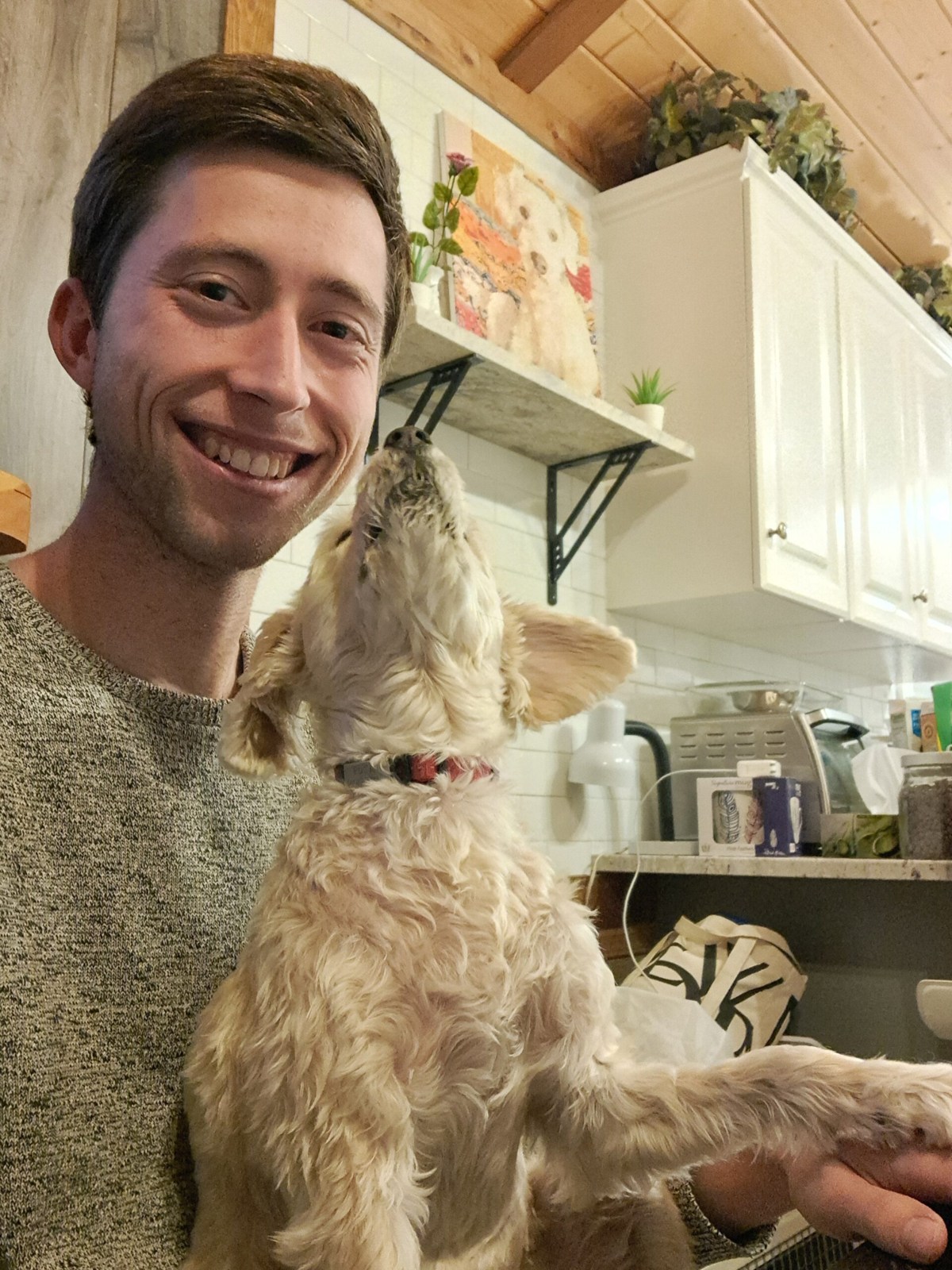 Lukas lächelt mit einem kleinen Hund auf dem Schoß in einer Küche.